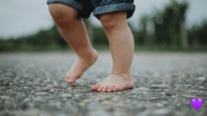 Primer plano de los pies descalzos de un niño caminando sobre el suelo, simbolizando los primeros pasos y el enfoque de Pilou para invertir con los pies en la tierra.